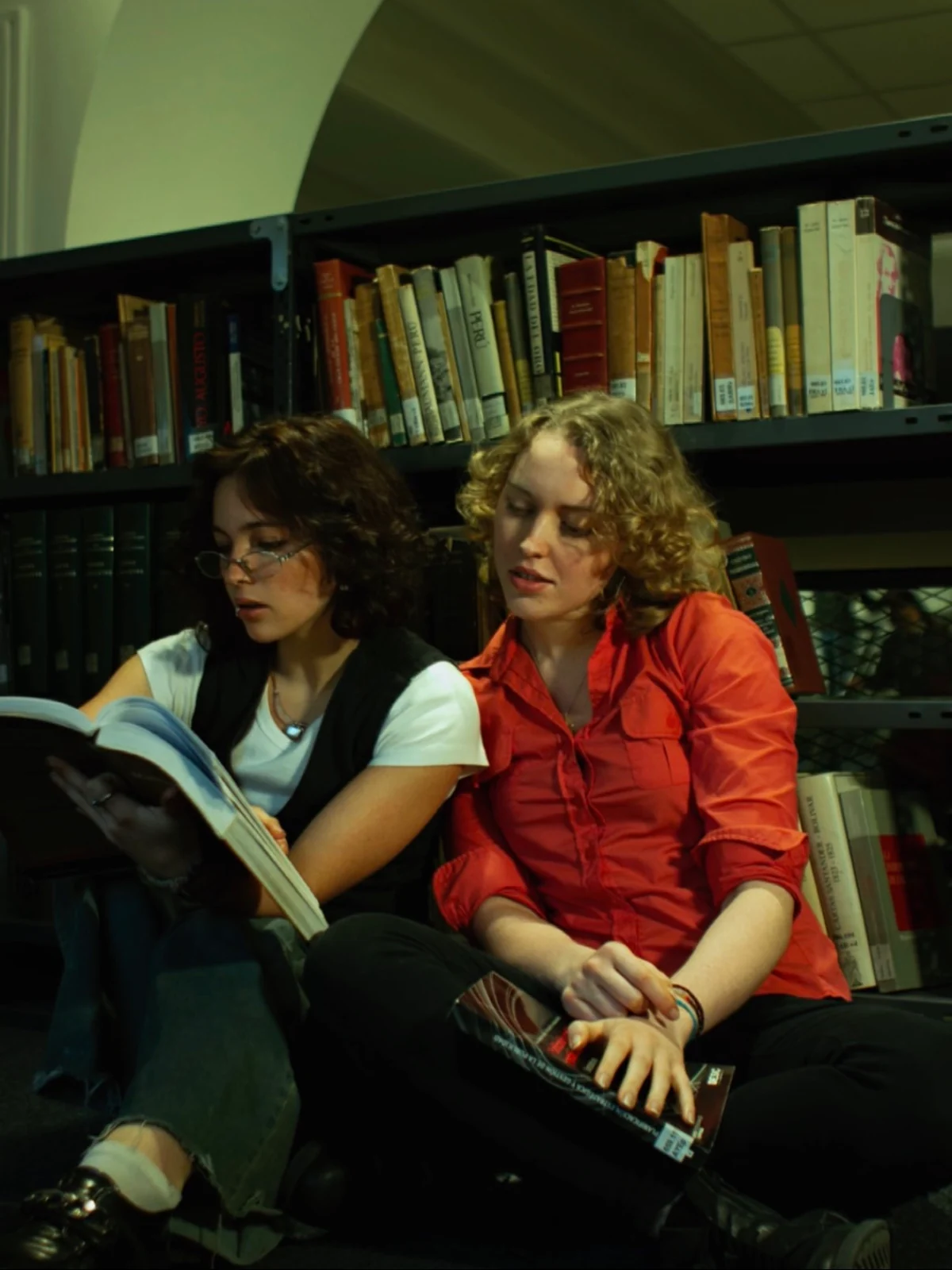Ju y Vic leen una revista en una biblioteca.